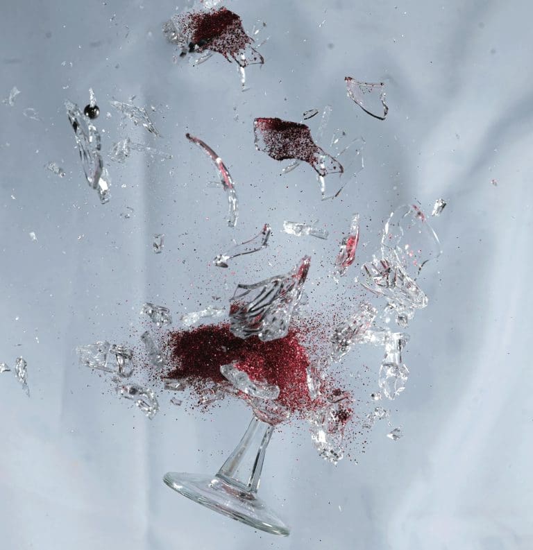 A mesmerizing display of a shattered wine glass with red glitters suspended in mid-air.